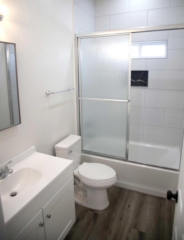 full bath featuring bath / shower combo with glass door, toilet, wood finished floors, and vanity