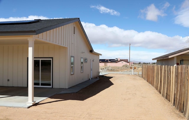 view of home's exterior with a patio area, roof with shingles, board and batten siding, and fence