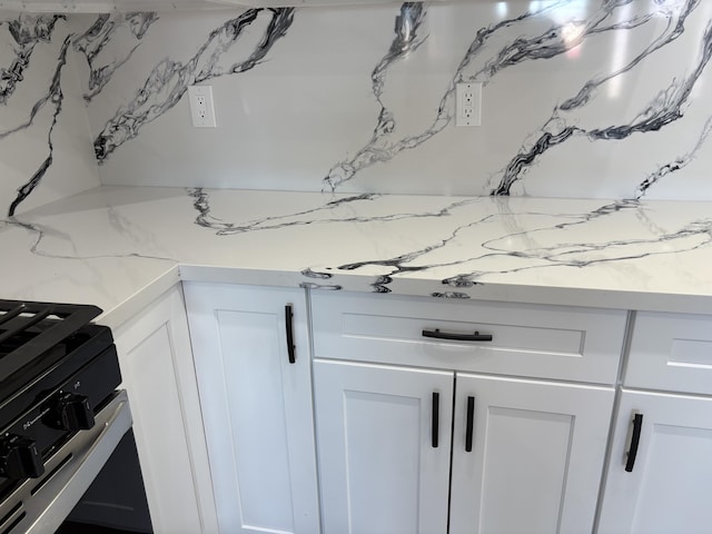 details with tasteful backsplash, white cabinets, light stone counters, and stainless steel gas stove