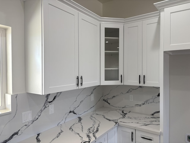interior space with white cabinets, glass insert cabinets, and backsplash