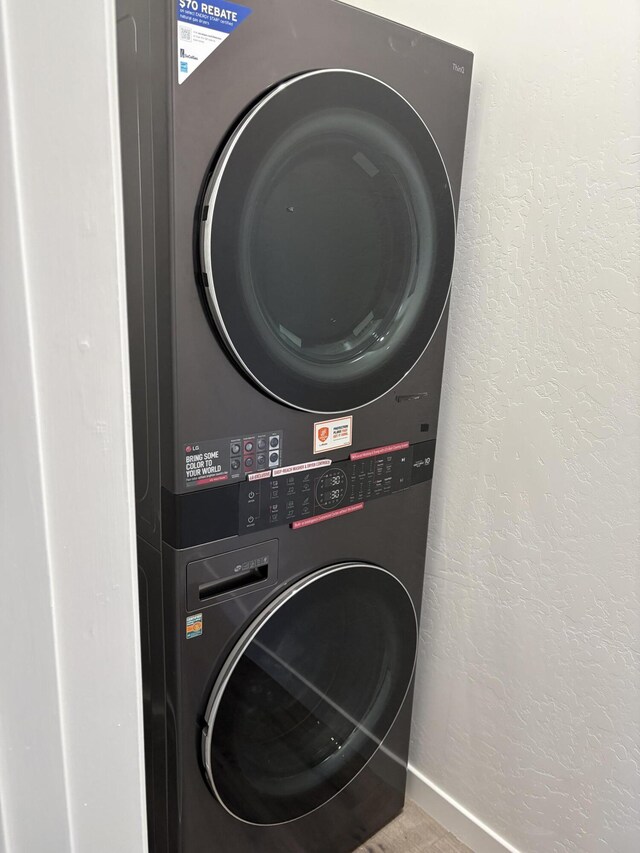 washroom with a textured wall, baseboards, laundry area, and stacked washer / dryer