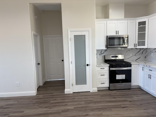 kitchen with appliances with stainless steel finishes, white cabinets, decorative backsplash, light stone countertops, and dark wood-style flooring