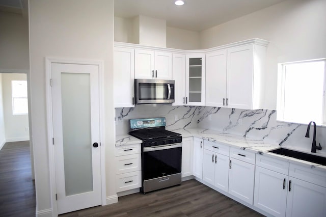 kitchen with a sink, backsplash, appliances with stainless steel finishes, white cabinets, and dark wood-style flooring