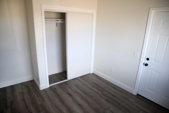 unfurnished bedroom with a closet, baseboards, and dark wood-type flooring