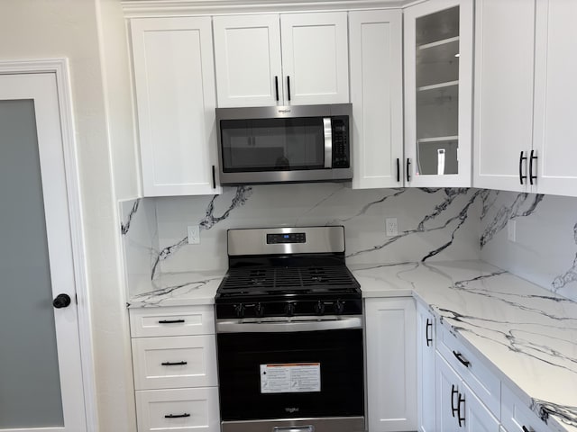 kitchen featuring glass insert cabinets, light stone countertops, decorative backsplash, appliances with stainless steel finishes, and white cabinets