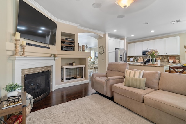 living room featuring wood finished floors, a fireplace, crown molding, visible vents, and arched walkways