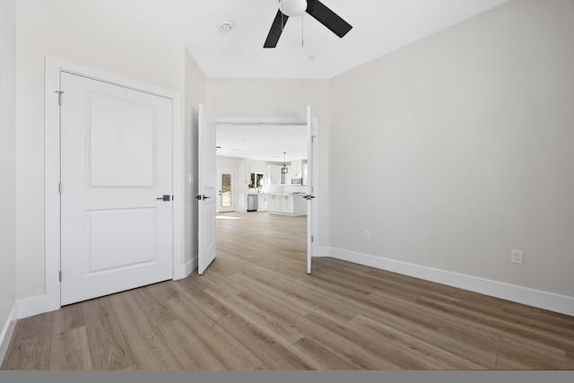 spare room with light wood finished floors, a ceiling fan, and baseboards