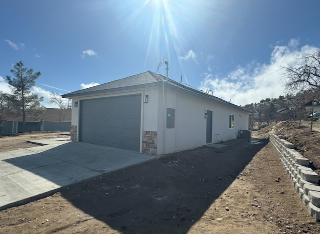 view of side of property featuring stucco siding, central AC unit, a garage, stone siding, and driveway