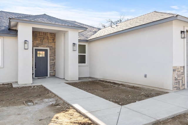 entrance to property featuring stone siding, roof with shingles, and stucco siding