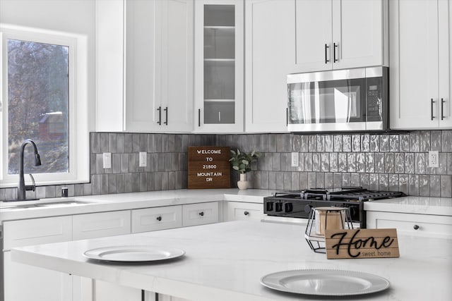 kitchen with plenty of natural light, stainless steel microwave, white cabinets, and decorative backsplash