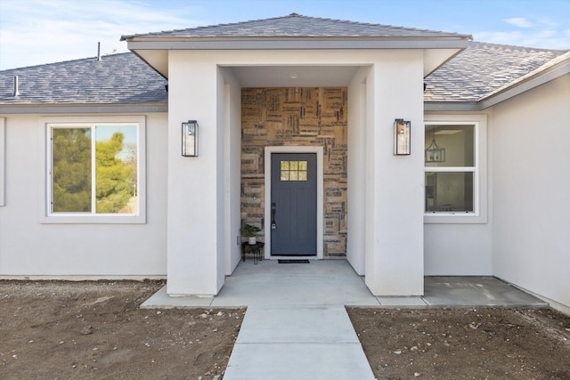 doorway to property with stone siding, a shingled roof, and stucco siding