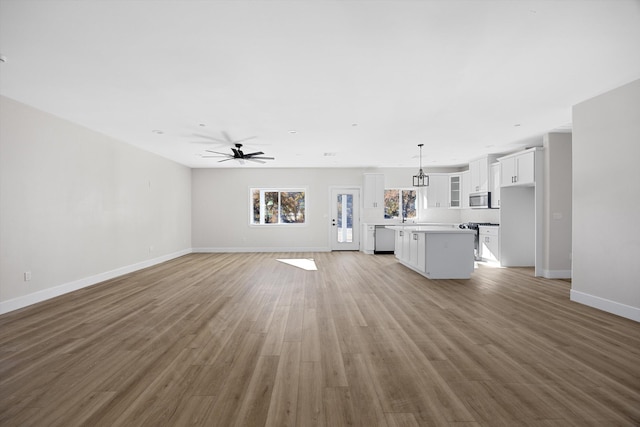 unfurnished living room with light wood-type flooring, baseboards, and a ceiling fan