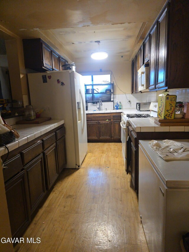 1239 W Rosecrans Ave Unit 31, Gardena, CA 90247 - kitchen with white appliances, light wood-style flooring, dark brown cabinets, tile countertops, and backsplash