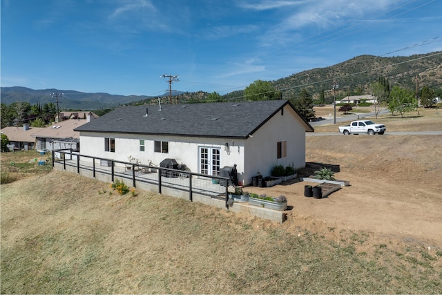 rear view of property featuring a mountain view, stucco siding, fence, and a shingled roof