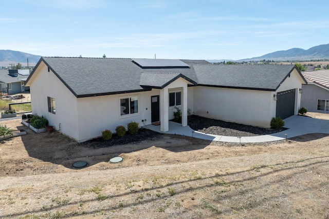 modern farmhouse with a mountain view, solar panels, stucco siding, a shingled roof, and a garage