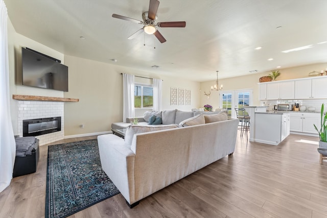 living room featuring a brick fireplace, a chandelier, light wood-style flooring, a ceiling fan, and recessed lighting