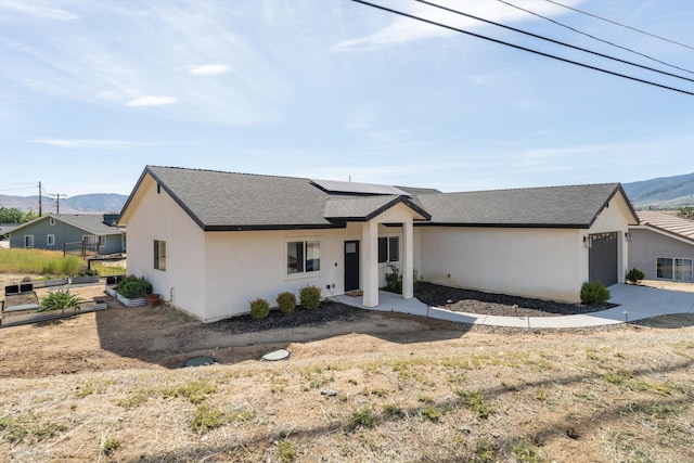 view of front of house featuring a mountain view, roof mounted solar panels, an attached garage, and stucco siding