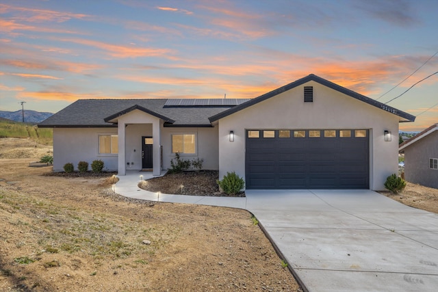 view of front of house featuring solar panels, an attached garage, stucco siding, driveway, and roof with shingles