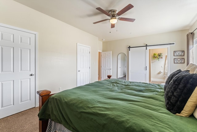 bedroom featuring a barn door, carpet floors, and a ceiling fan