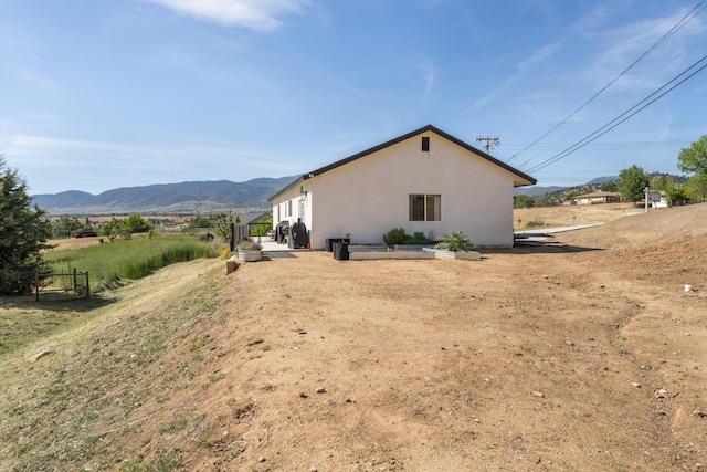 view of side of home featuring stucco siding, a mountain view, and fence