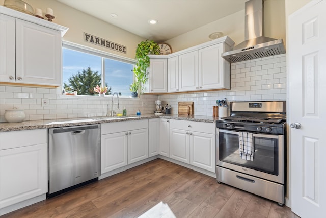 kitchen featuring appliances with stainless steel finishes, wall chimney exhaust hood, a sink, recessed lighting, and white cabinets