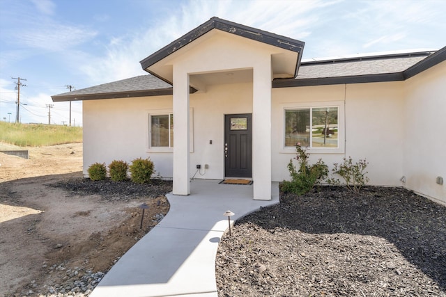 entrance to property with stucco siding, solar panels, and a shingled roof