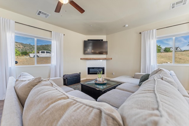 living room featuring plenty of natural light, a ceiling fan, a fireplace, and wood finished floors