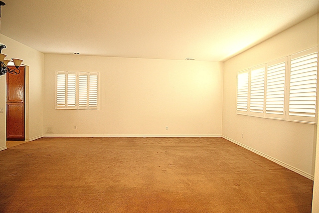 carpeted empty room featuring a notable chandelier and a healthy amount of sunlight