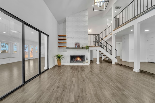 unfurnished living room with a brick fireplace, wood-type flooring, and high vaulted ceiling