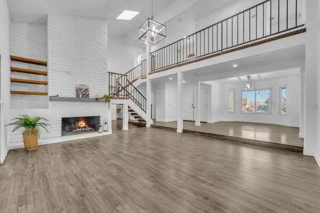 unfurnished living room with high vaulted ceiling, a fireplace, a chandelier, and hardwood / wood-style floors