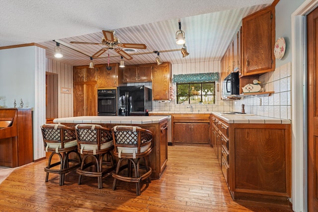 2600 Aland St, Lancaster, CA 93536 - kitchen featuring tile countertops, black appliances, light wood-style floors, and decorative backsplash