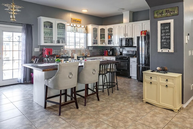 kitchen with tasteful backsplash, a center island with sink, light tile patterned floors, and black appliances
