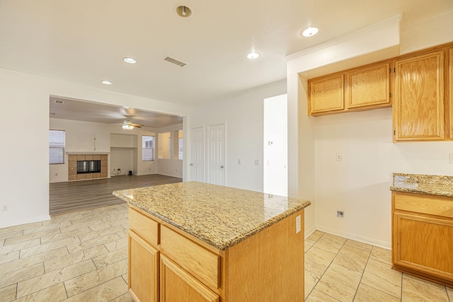 kitchen with a center island, visible vents, a tiled fireplace, ceiling fan, and light stone countertops