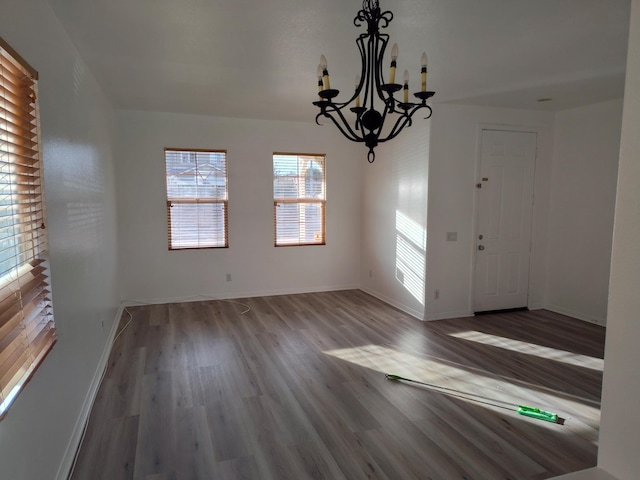 unfurnished dining area featuring baseboards, a chandelier, and wood finished floors