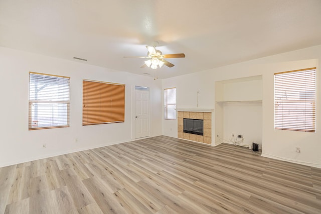unfurnished living room with light wood finished floors, visible vents, a tiled fireplace, ceiling fan, and baseboards