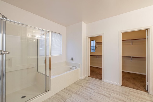 full bath featuring a garden tub, a spacious closet, a shower stall, and baseboards