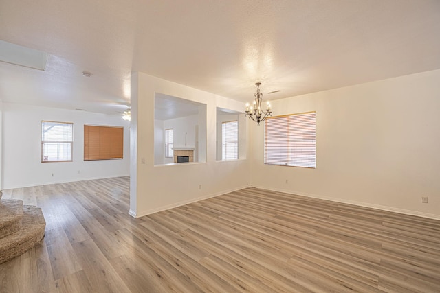 empty room featuring baseboards, light wood-style flooring, a tiled fireplace, and ceiling fan with notable chandelier