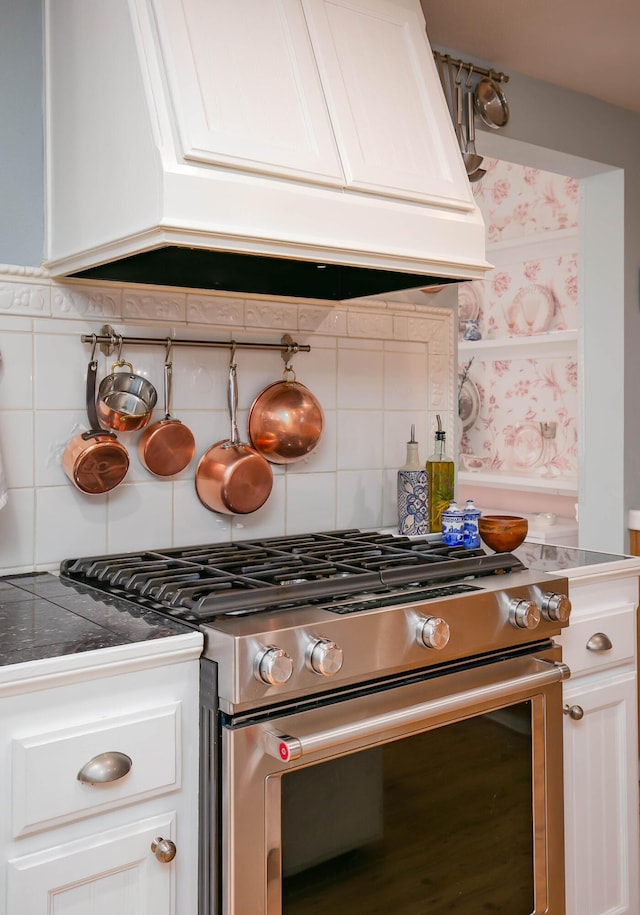 kitchen featuring tasteful backsplash, custom range hood, white cabinets, and stainless steel gas stove