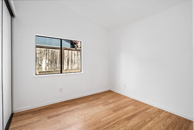 empty room with baseboards, vaulted ceiling, and light wood-style floors