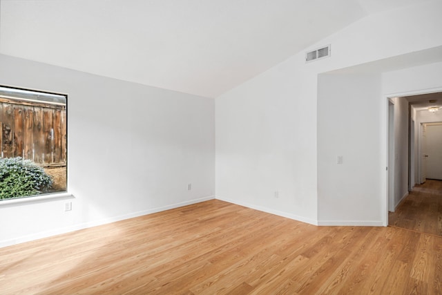 unfurnished room featuring baseboards, visible vents, vaulted ceiling, and wood finished floors