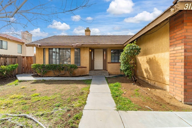 property entrance with a tiled roof, a chimney, fence, and stucco siding