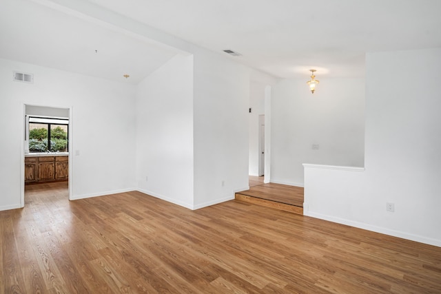 unfurnished room with vaulted ceiling, wood finished floors, visible vents, and baseboards