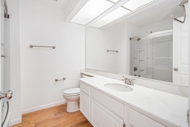 bathroom featuring toilet, vanity, wood finished floors, and a shower with shower door