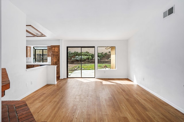 unfurnished living room with light wood-type flooring, baseboards, and visible vents