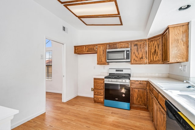 kitchen with stainless steel appliances, visible vents, brown cabinetry, vaulted ceiling, and light wood-type flooring