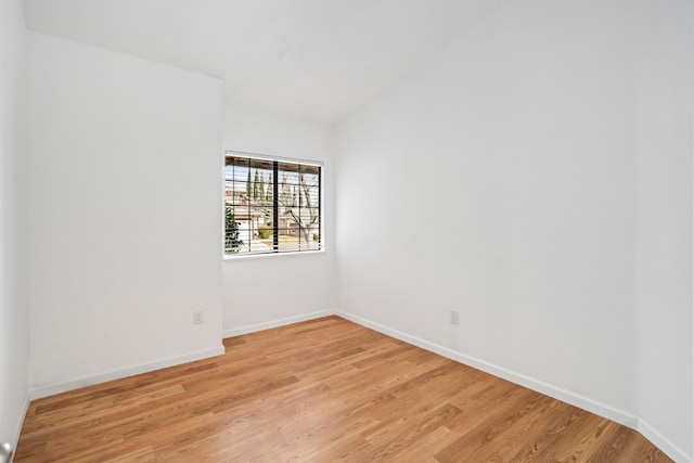 spare room with light wood-type flooring, baseboards, and vaulted ceiling