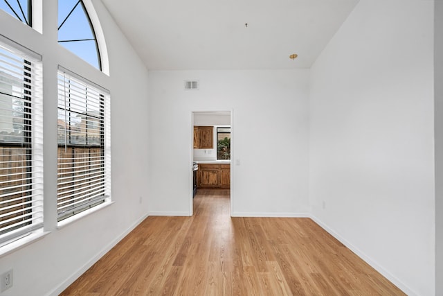 spare room featuring high vaulted ceiling, light wood-style flooring, visible vents, and baseboards