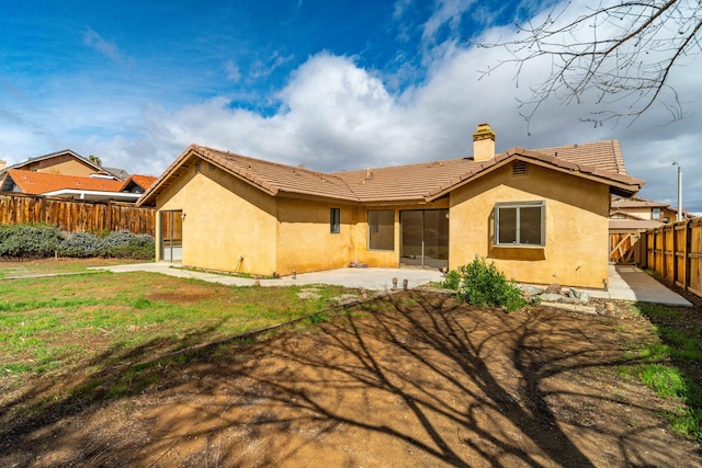 rear view of house with a fenced backyard, a chimney, a tiled roof, a patio area, and stucco siding