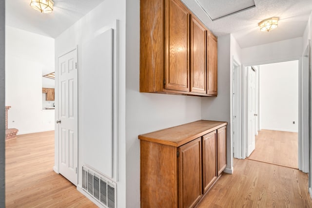 hallway featuring a textured ceiling, light wood-style flooring, visible vents, and baseboards