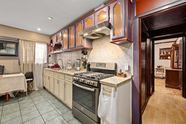 kitchen featuring sink, stainless steel gas range, decorative backsplash, range hood, and cream cabinetry